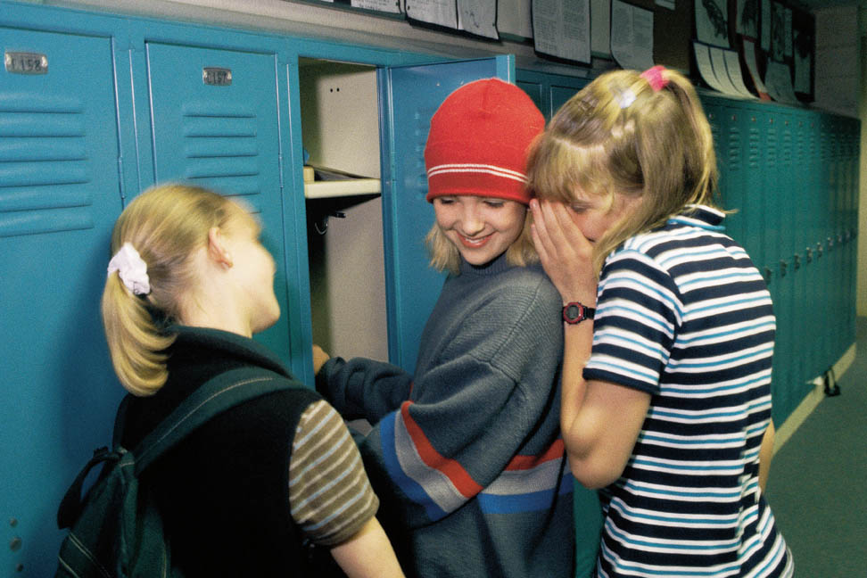 three girls wispering to eachother in the hallway at school