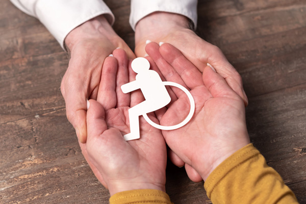Two person holding a cutout of a disability signal on its palm hands