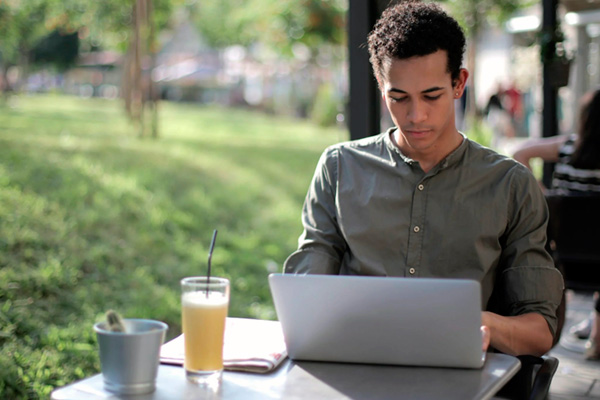 A young man using its laptop while enjoying of a fresh beverage.