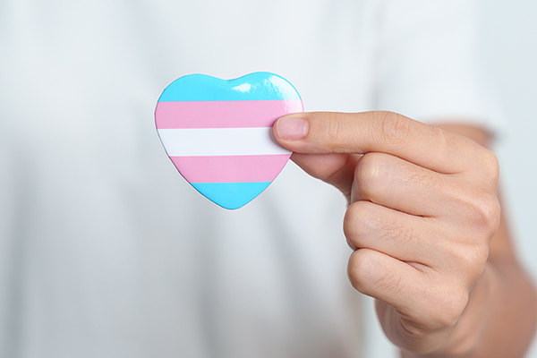 A person holding up a heart pin with the transgender flag on it.