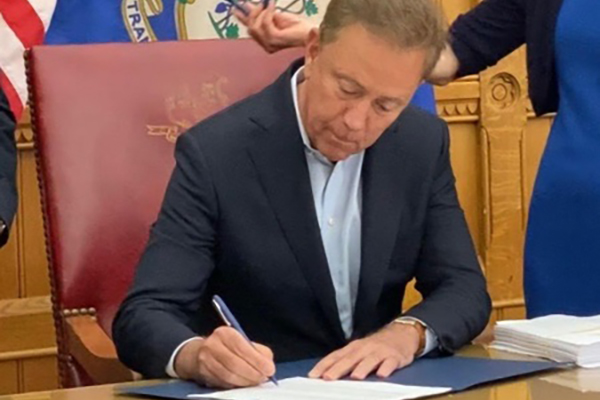 Governor Lamont signing an Executive Order at his desk.