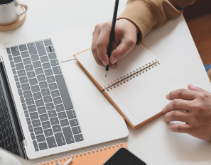 Hands writing in a notebook with keyboard in front